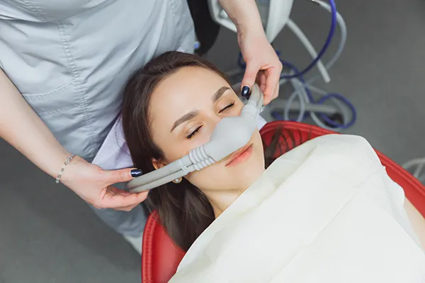 Dental assistant fitting a sedation mask over the nose of her calm female patient during wisdom teeth removal at Downey Oral and Maxillofacial Surgery in Downey, CA